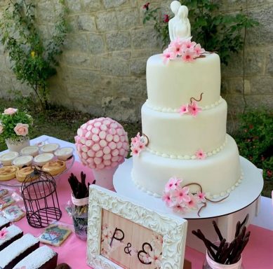 TARTA DE BODA Tarta blanca de tres pisos decorada con flores y figuras de novios, acompañada de dulces.