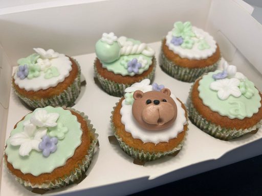 CUPCAKES PARA BABY SHOWER Seis cupcakes decorados con crema verde, flores y un oso de chocolate en la parte superior.
