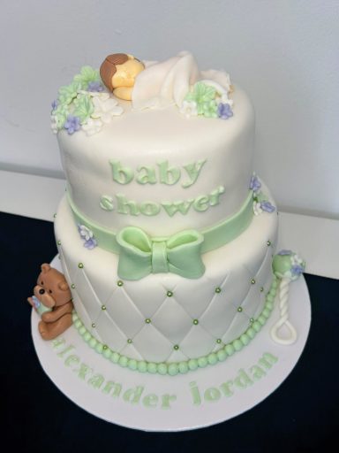 BABY SHOWER Pastel de bebé de dos pisos con un muñeco durmiendo y decoraciones en tonos verde y azul.