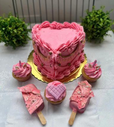 TARTA Y DULCES VINTAGE Pastel en forma de corazón rosa con cupcakes y helados decorativos alrededor.