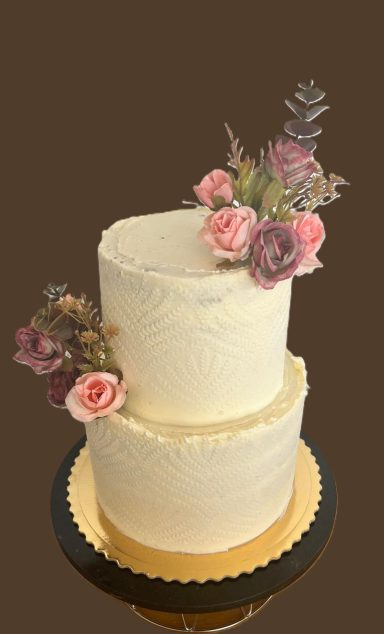 TARTA DE BODA Tarta de dos pisos decorada con flores rosas y moradas en un fondo marrón.