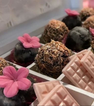 MESA TEMÁTICA DE COMUNIÓN Bombones decorados con flores y tabletas de chocolate en una caja.