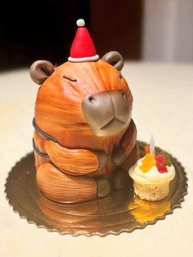 TARTA 3D CAPIBARA Tarta en forma de un capibara con gorro navideño y cupcake al lado.