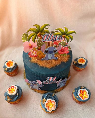 TARTA STITCH Y CUPCAKES Tarta de cumpleaños con tema de "Lilo y Stitch", decorada con flores y palmeras.