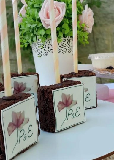 BROWNIES DE BODA Dulces de chocolate decorados con flores y palitos de papel en una mesa festiva.