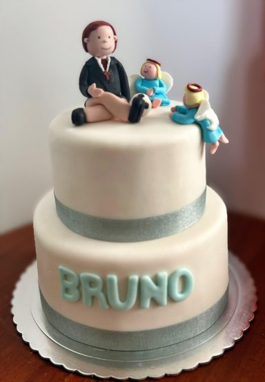TARTA DE COMUNIÓN Tarta de dos pisos decorada con figuras de un hombre y dos bebés, con el nombre "BRUNO".